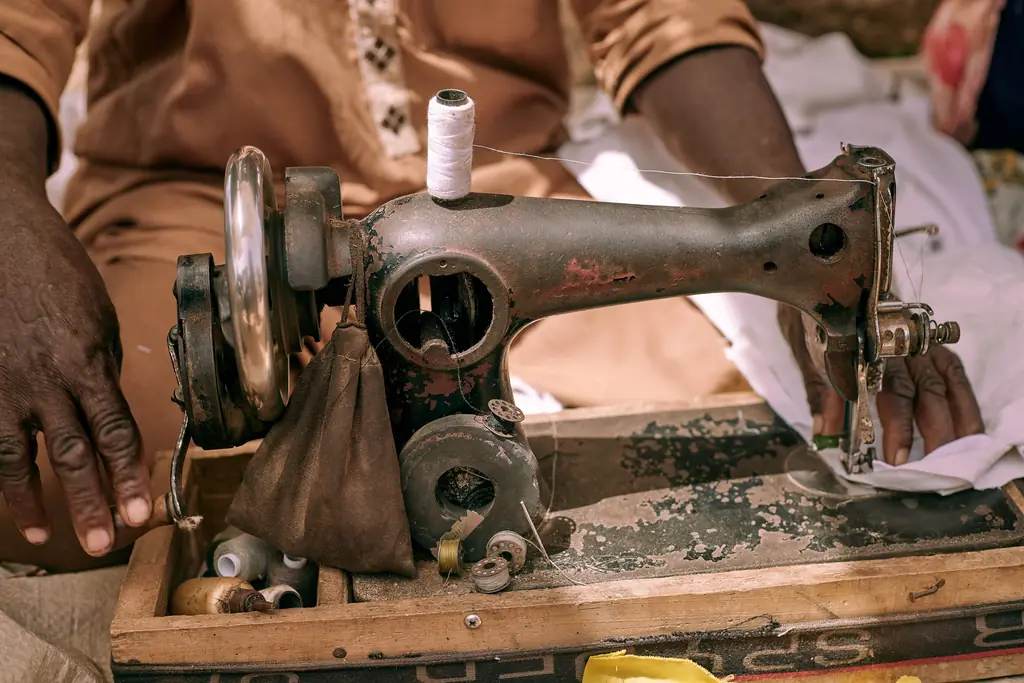 Les mains d’un artisan sur une vieille machine à coudre, en plein air.