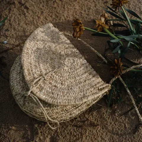 Sac en raphia tressé posé sur le sable.